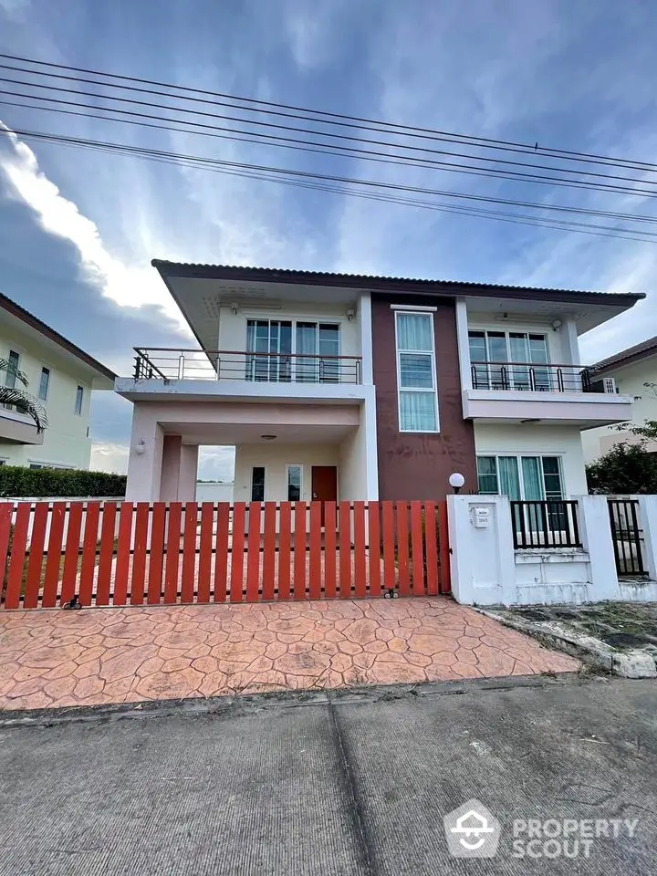 Modern two-story house with balcony and red fence in a suburban neighborhood.