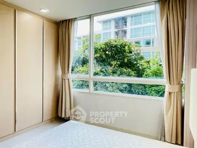 Bright bedroom with large window offering lush garden view in modern apartment.