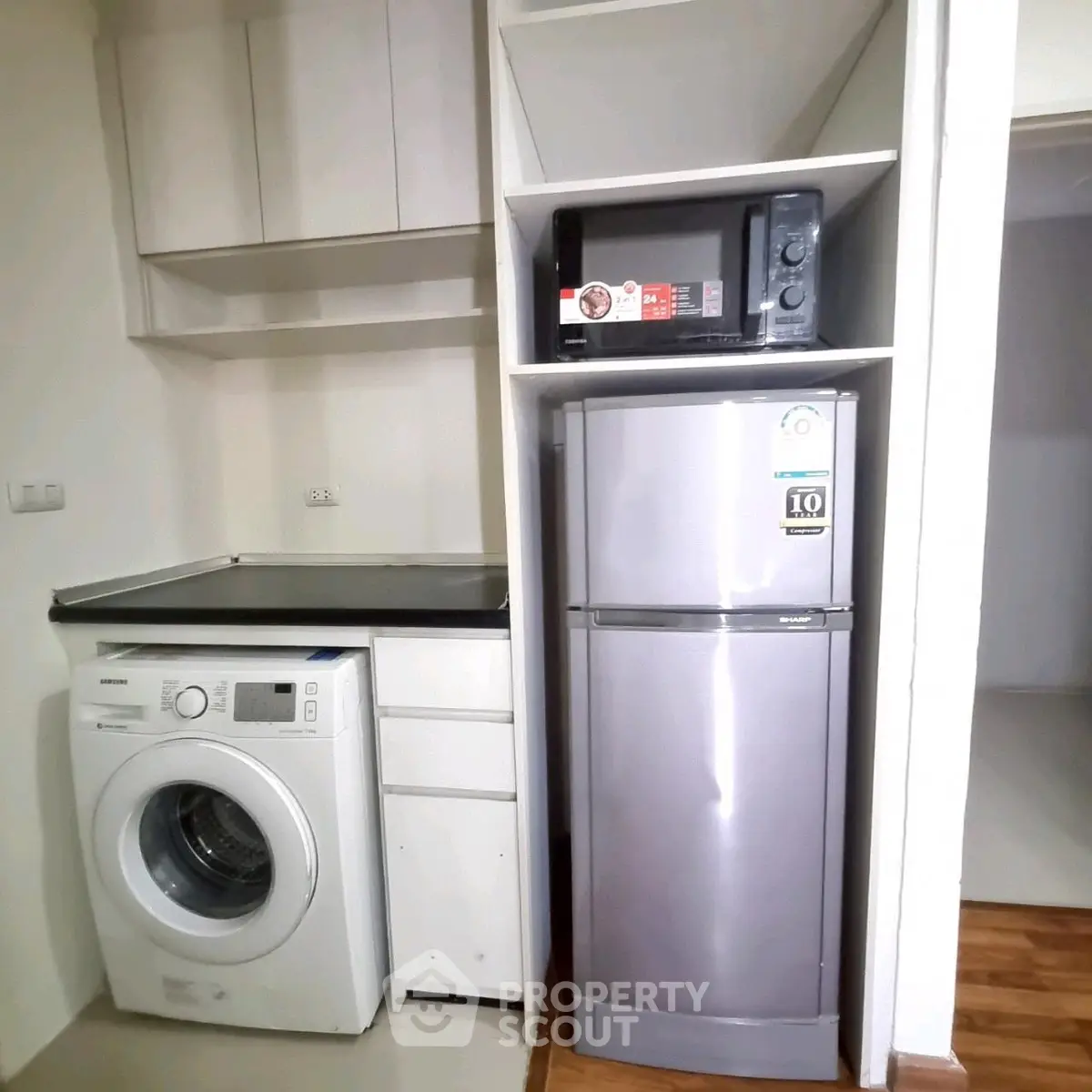 Compact laundry and kitchen area with washing machine, fridge, and microwave in modern apartment.
