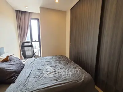 Cozy bedroom with modern decor and ample natural light from large window.