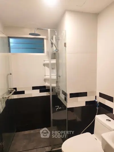 Modern bathroom with glass shower enclosure and sleek black and white tiles.