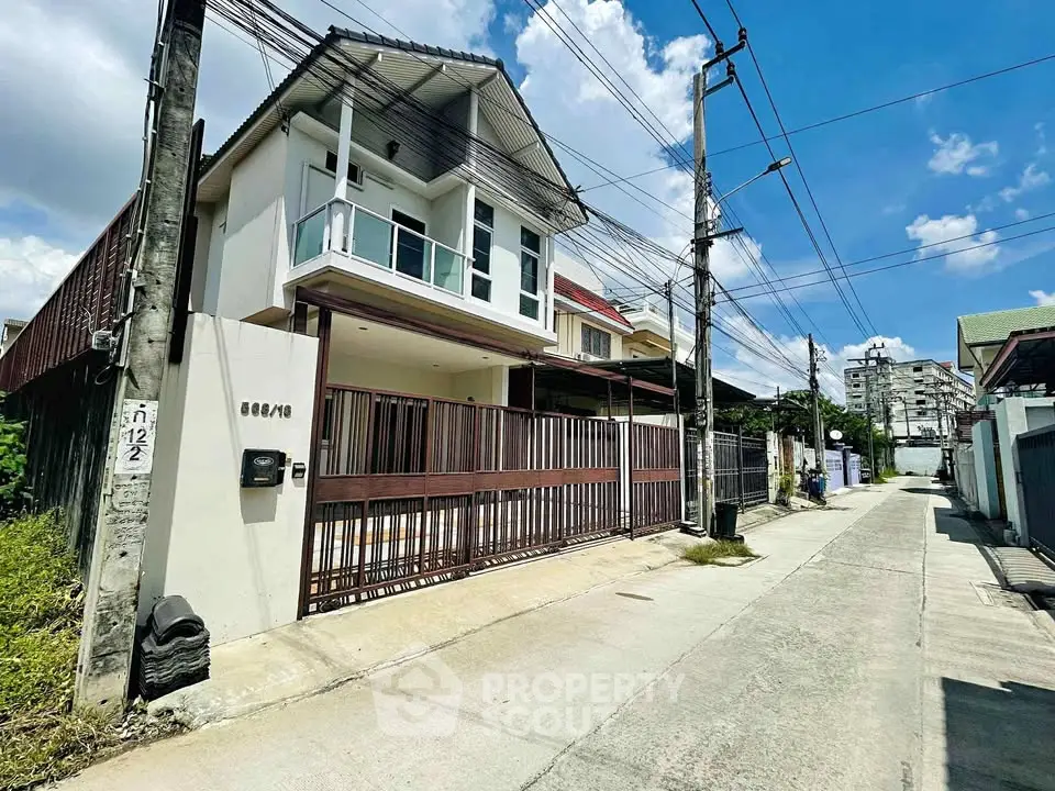 Modern two-story house with balcony and gated entrance in a suburban neighborhood.
