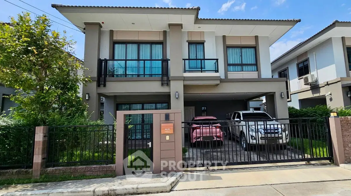 Modern two-story house with gated driveway and two cars parked in front.