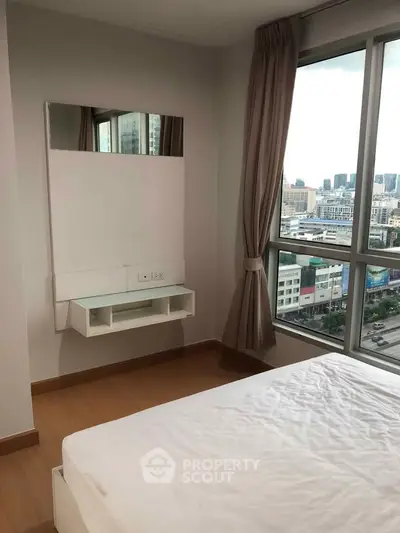 Modern bedroom with large window offering city view, featuring minimalist decor and natural light.