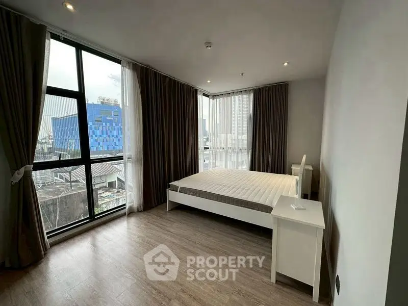 Spacious bedroom with large windows and modern decor in urban apartment.