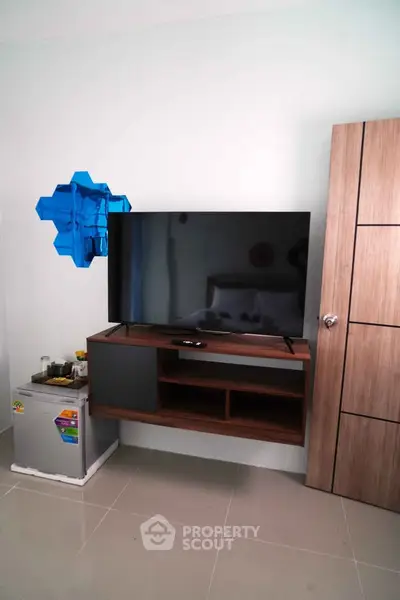Modern living room with sleek TV setup and compact fridge, ideal for cozy urban living.