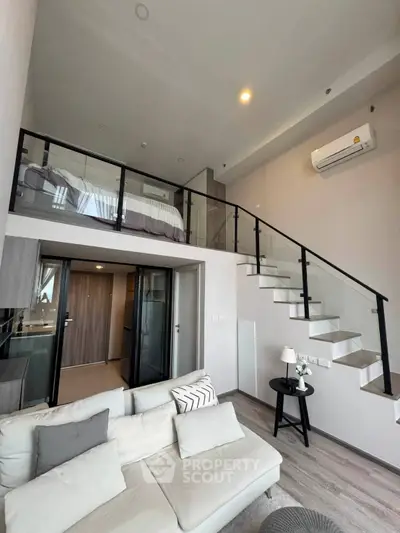 Modern loft apartment with stylish mezzanine bedroom and open living area, featuring sleek glass railing and cozy decor.