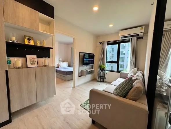 Modern living room with cozy sofa, wall-mounted TV, and view into a stylish bedroom in a contemporary apartment.