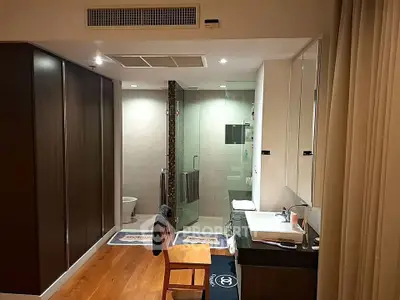 Modern bathroom with glass shower, wooden flooring, and sleek vanity in a stylish apartment.