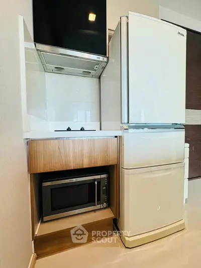 Modern kitchen with fridge, microwave, and gas stove in compact layout.