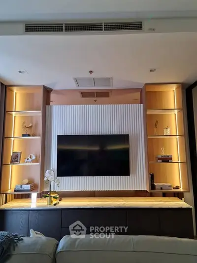 Modern living room with built-in shelves and mounted TV, featuring elegant lighting and decor.