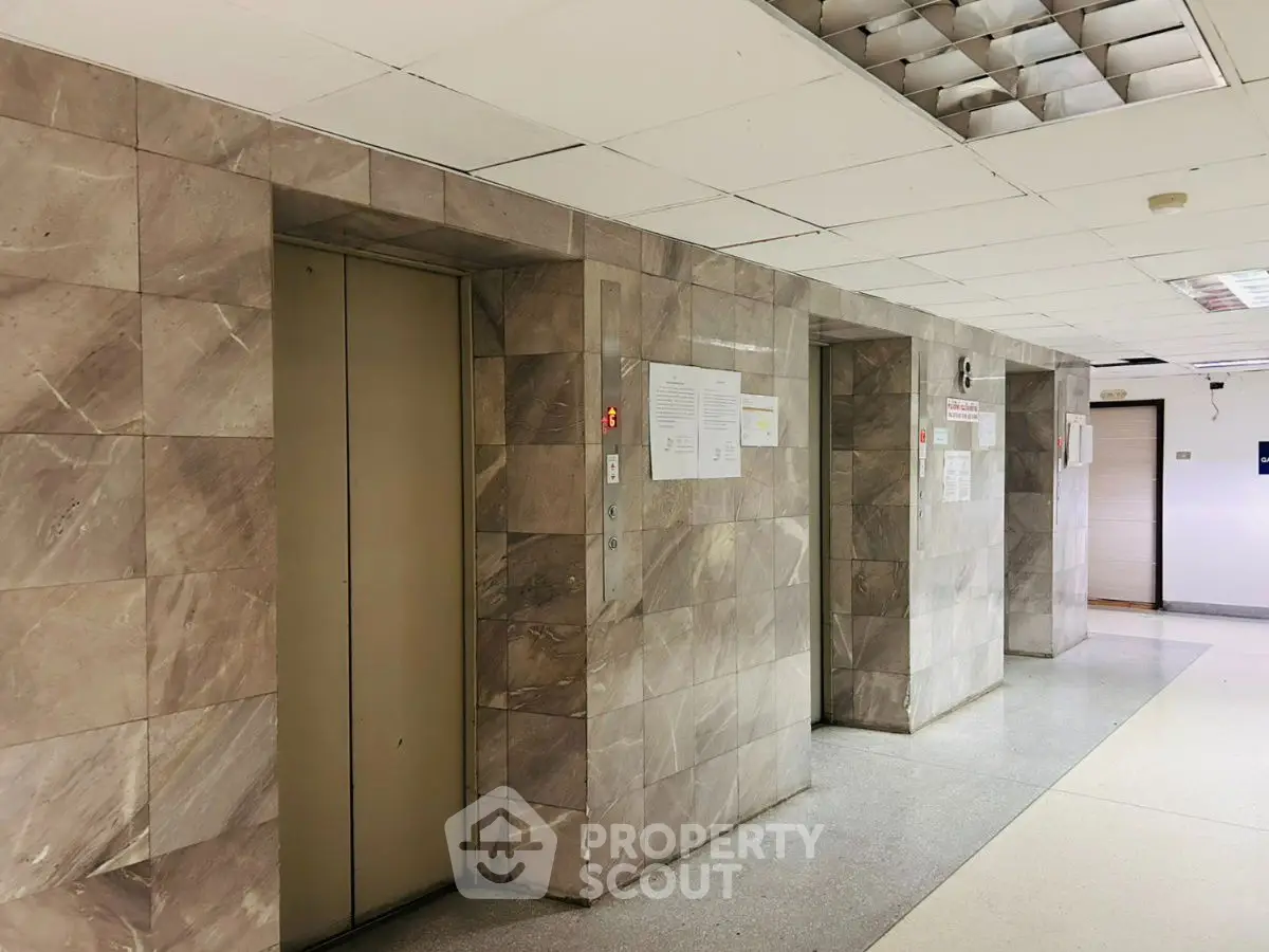 Spacious building hallway with elevator access and modern tiled walls.