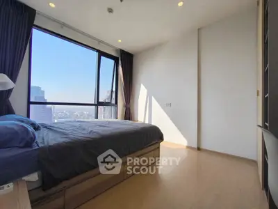 Spacious bedroom with large window offering stunning city views in modern apartment.