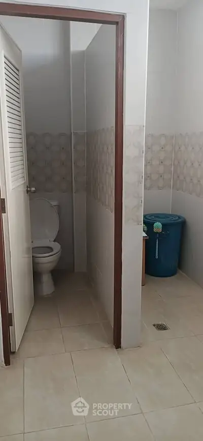 Compact bathroom with tiled walls and floor, featuring a toilet and a blue water container.