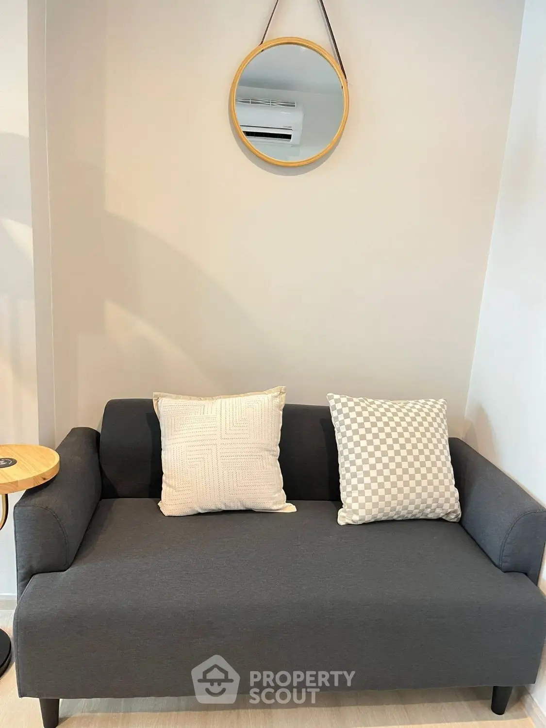 Modern living room with stylish gray sofa and decorative pillows under a round mirror.
