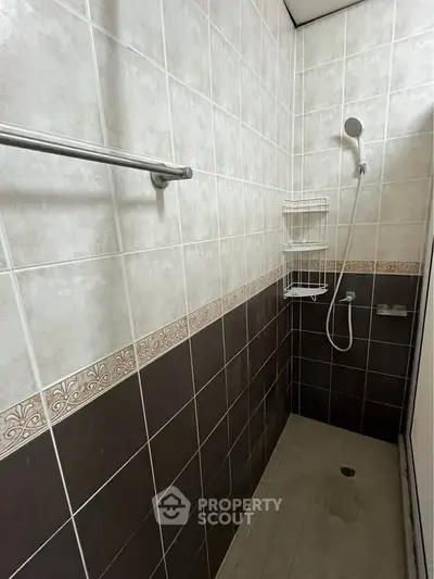 Compact bathroom with tiled walls and shower area, featuring a sleek showerhead and towel rack.
