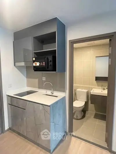 Modern compact kitchen with sleek cabinetry and adjacent bathroom in a contemporary apartment.