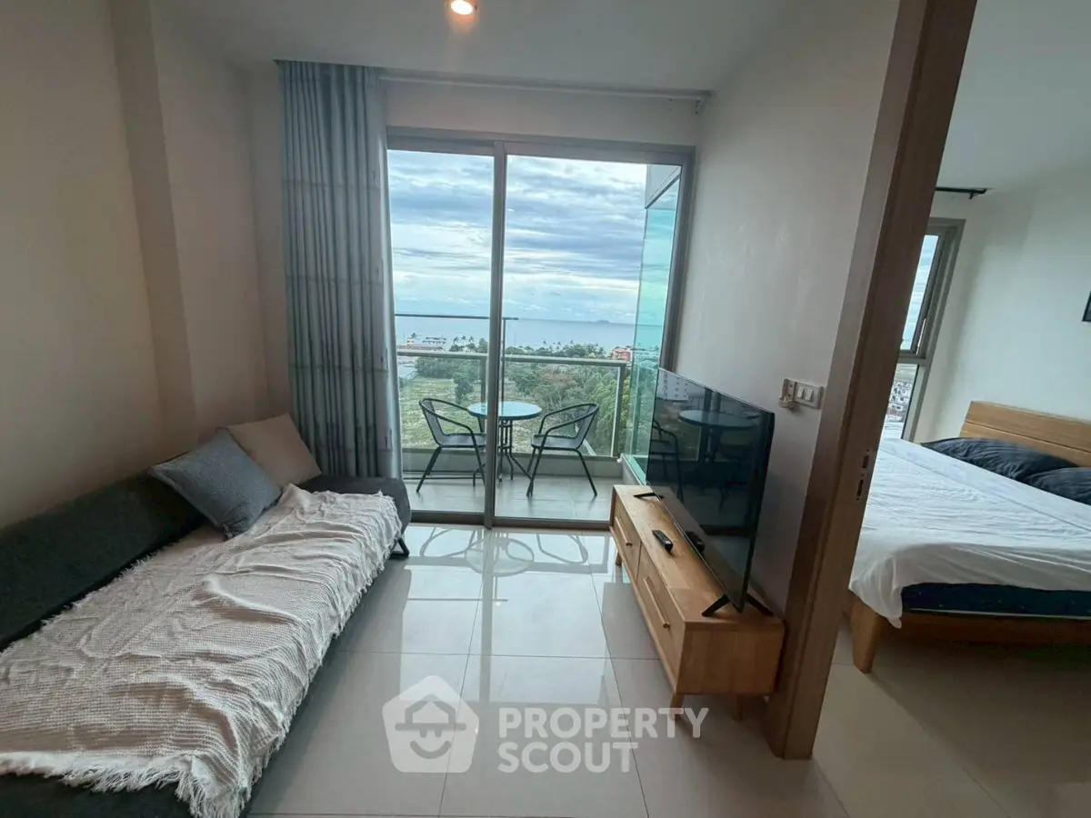 Modern living room with balcony and ocean view, adjacent to cozy bedroom.
