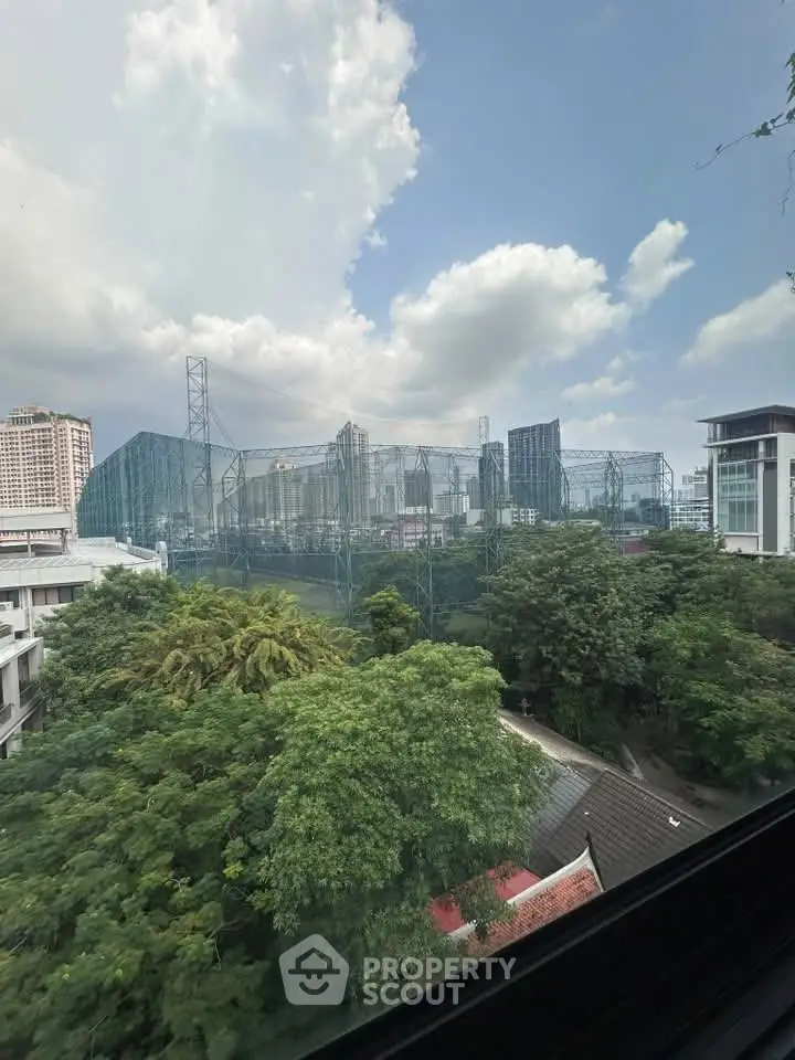 Stunning cityscape view from a high-rise window overlooking lush greenery and urban skyline.