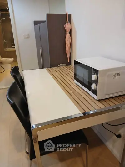 Modern kitchen with sleek table, chairs, and microwave, adjacent to a bathroom, showcasing compact urban living.