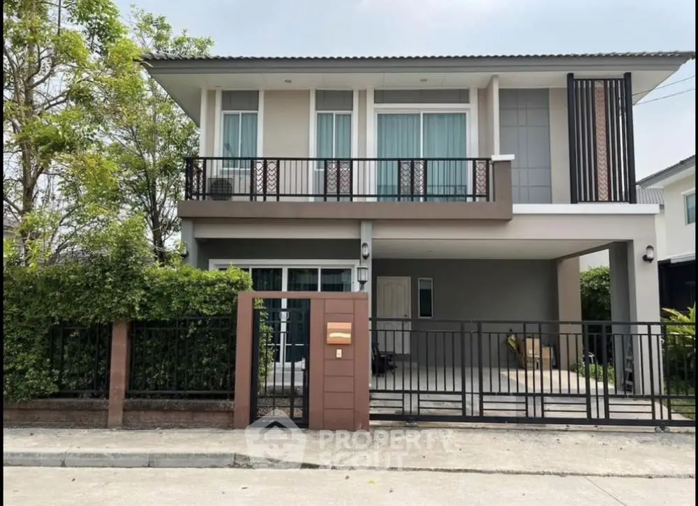 Modern two-story house with balcony and gated entrance in suburban setting.