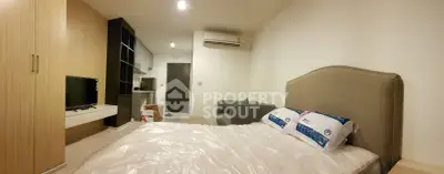 Modern studio apartment with cozy bedroom and compact kitchen, featuring sleek furniture and neutral tones.