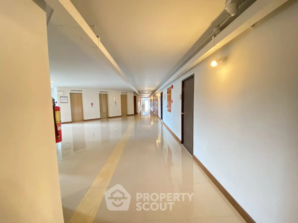 Spacious and well-lit corridor in modern apartment building with polished floors.