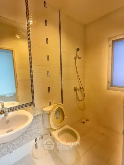 Modern bathroom with shower, toilet, and sink in a bright, tiled space.