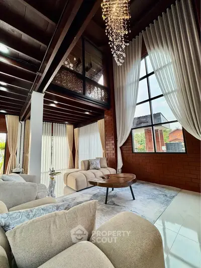 Luxurious living room with high ceilings, elegant chandelier, and large windows offering natural light.