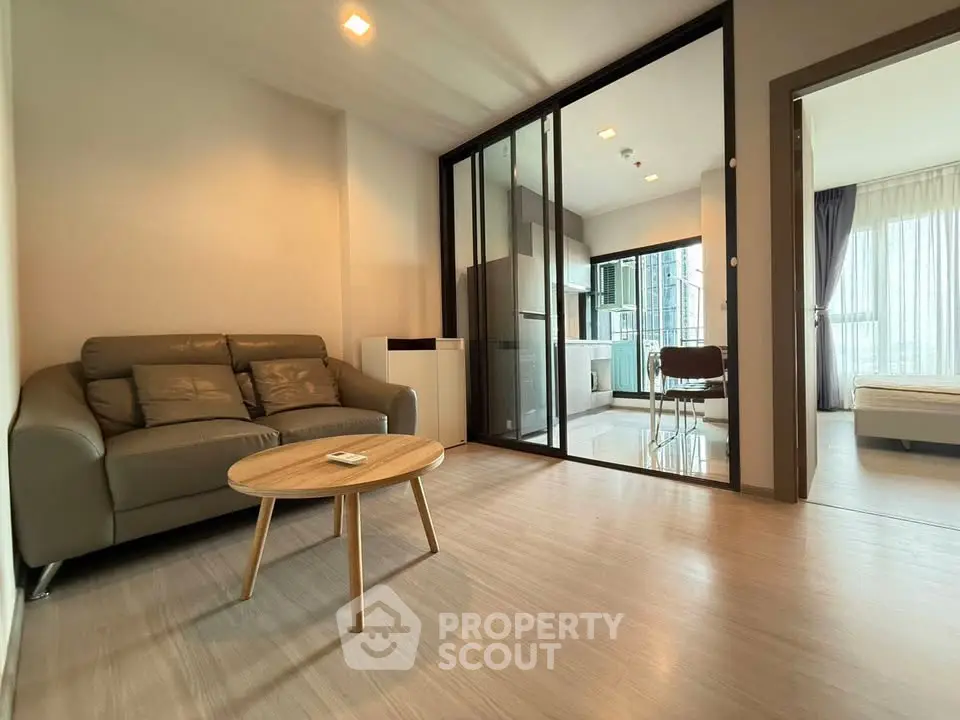 Modern living room with open layout and glass partition leading to kitchen and bedroom.