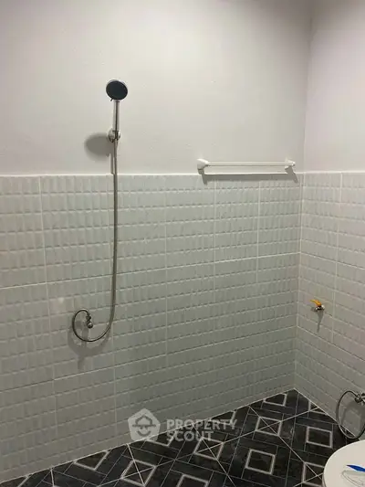 Minimalist bathroom with tiled walls and floor, featuring a shower head and towel rack.