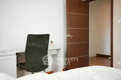 Modern bedroom with sleek desk and chair, open door leading to hallway.