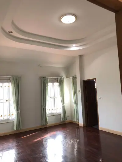 Spacious room with elegant ceiling design and large windows with green curtains.