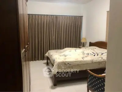 Cozy bedroom with elegant wooden furniture and large window draped with curtains, perfect for relaxation.