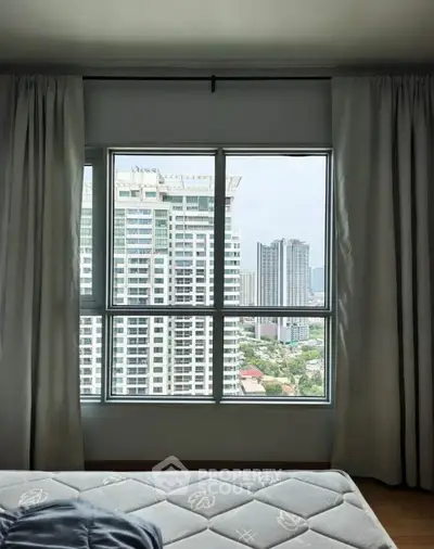 Spacious bedroom with large window offering stunning city view in modern apartment.