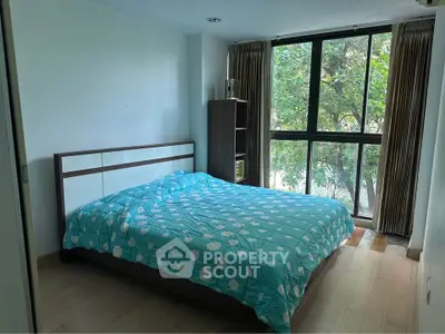 Cozy bedroom with large window and tree view, featuring a comfortable bed and wooden flooring.