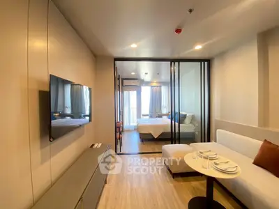 Modern apartment interior with open living room and bedroom, featuring sleek design and natural light.