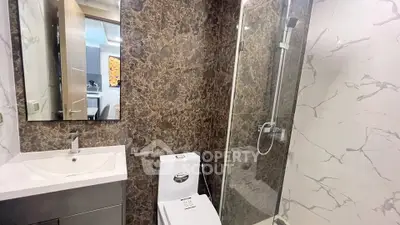 Modern bathroom with marble walls and glass shower enclosure in luxury apartment.