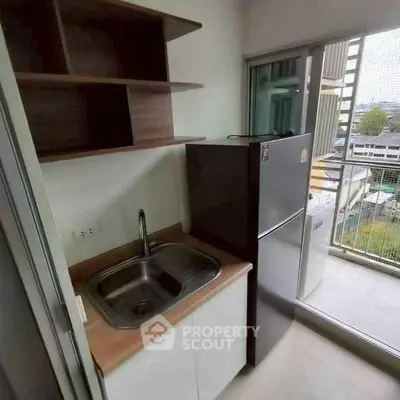 Compact kitchen with sink and fridge adjacent to balcony with city view.