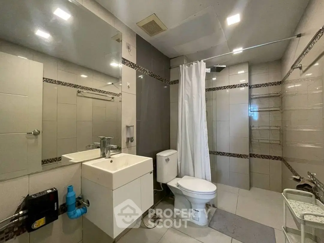 Modern bathroom with sleek fixtures and neutral tiles, featuring a shower and vanity unit.