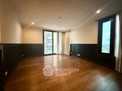 Spacious empty living room with wooden flooring and large windows offering city views.