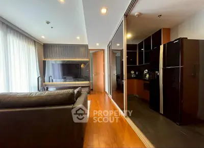 Modern living room with sleek kitchen and large fridge, featuring wooden flooring and stylish lighting.