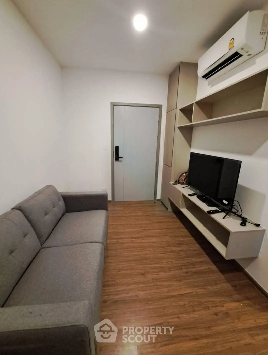 Cozy living room with modern sofa, TV, and air conditioning in a compact apartment.