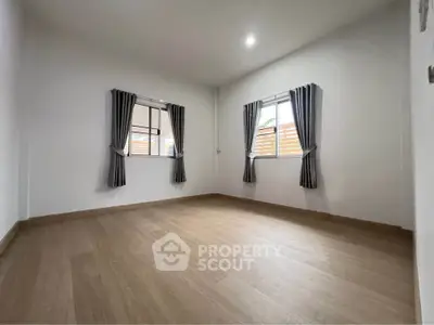Spacious empty room with wooden flooring and two windows, perfect for customization.