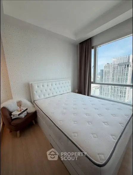 Modern bedroom with city view, featuring a stylish bed and cozy chair, perfect for urban living.