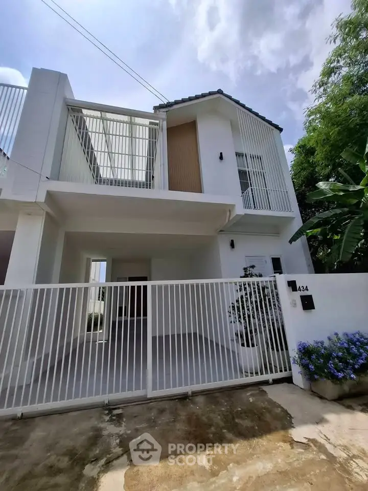 Modern white two-story house with gated entrance and lush greenery