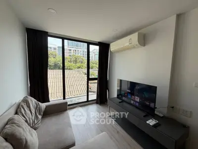 Modern living room with large windows and city view, featuring a cozy sofa and sleek TV setup.