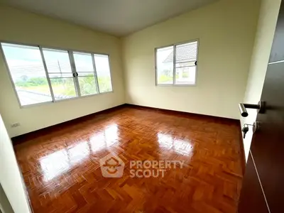 Spacious bedroom with polished wooden floors and large windows offering natural light.