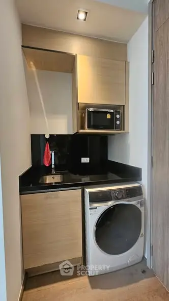 Compact kitchen with modern appliances including washing machine and microwave, ideal for urban living.