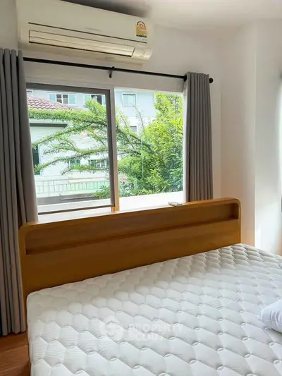 Bright bedroom with large window and air conditioning, showcasing a comfortable bed and serene outdoor view.